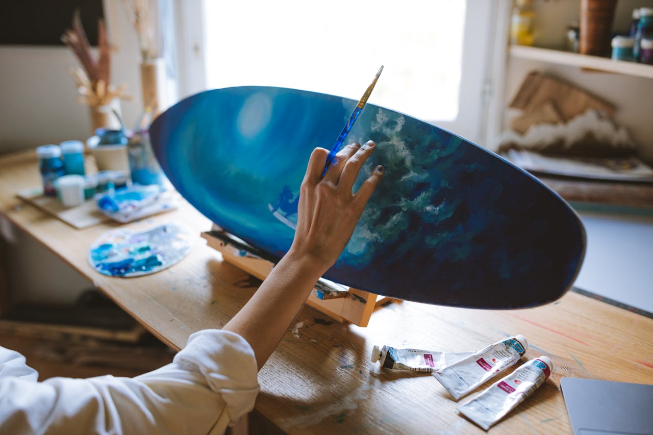 Close-up of an artist painting a surf-themed surfboard in a creative studio setting.